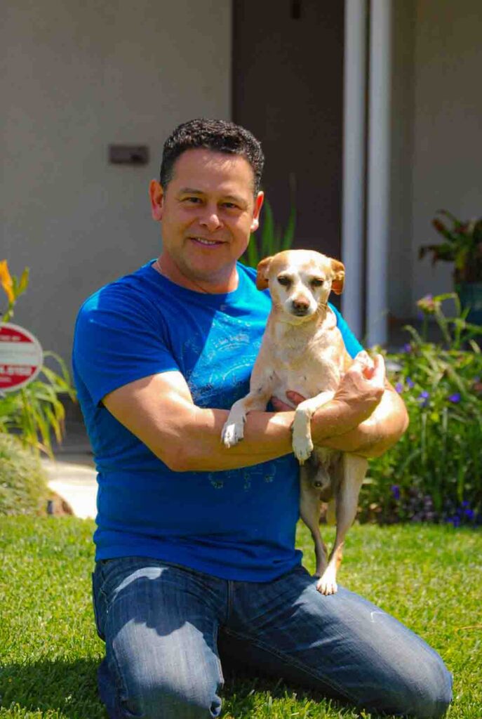 USAKARA's Founder: Caesar Muñoz holding one of our rescued dogs named buddy woods. He's a small white and golden brown dog.